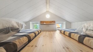 A room with two beds, wooden floors, a sloped ceiling, and a window with a view.