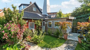 A house with a sloped roof, a chimney, and a garden with various plants and flowers.