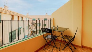 Ein Balkon mit Tisch und Stühlen, Blick auf Gebäude und ein Maschendrahtzaun.