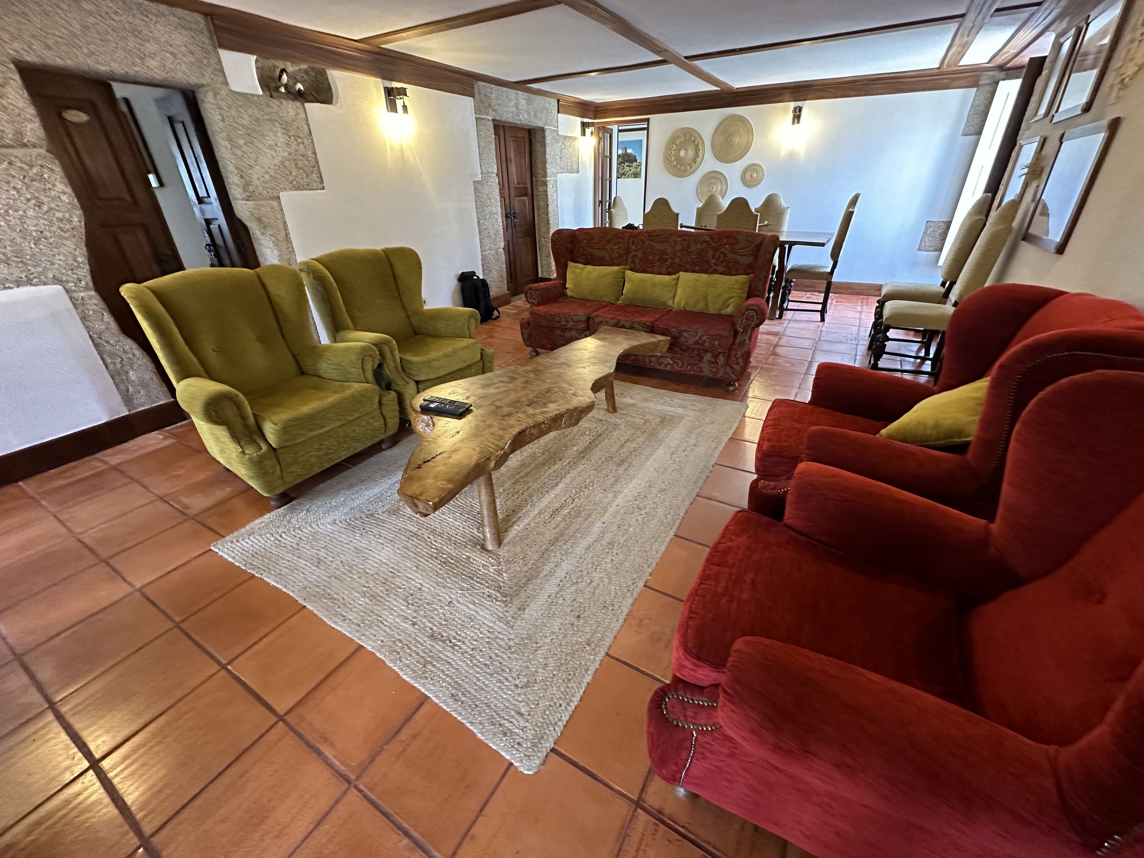 Een ruime woonkamer met een houten salontafel, groene en rode fauteuils en een gestreept bankstel.