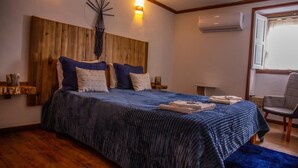 Een slaapkamer met een houten hoofdbord, een groot bed met blauw beddengoed, een stoel en een airconditioning.