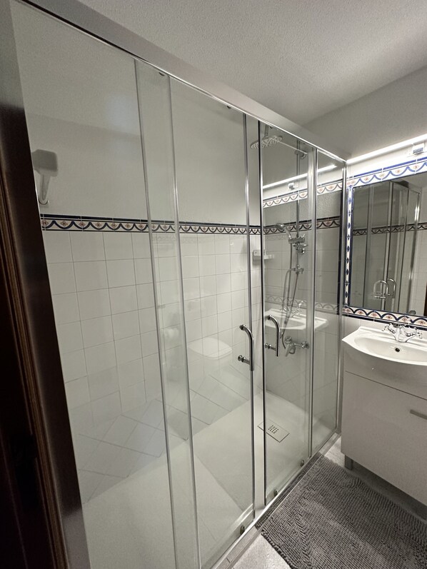 A modern bathroom with a glass shower enclosure, a white sink, and a mirror with a decorative tile border.