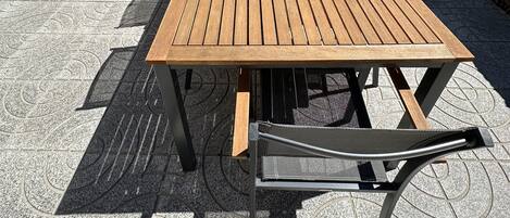 A wooden table with chairs, a stone wall, and a grill in the background.