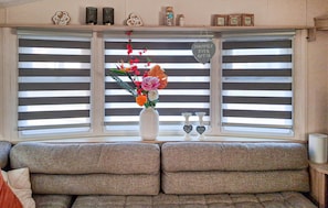 A room with a window with horizontal blinds, a white vase with flowers, two heart-shaped signs, and a shelf with decorative items. - 2 bedroom amazing home in Makkum (Makkum)