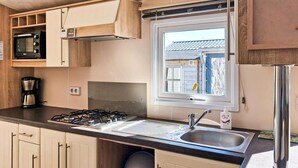 Een kleine keuken met een gasfornuis, een spoelbak en een raam met uitzicht op een woonwijk.