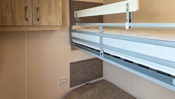 Een stapelbed met hoofdbord, bevestigd aan een muur, een klein plankje eronder en een stopcontact in de muur.