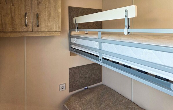 A bunk bed with a headboard attached to a wall, a small shelf below, and a power outlet on the wall.