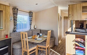 Cocina compacta para autocaravana con comedor, armarios de madera y ventana con cortinas.