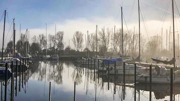 Een jachthaven met aangemeerde boten, stil water en kale bomen op de achtergrond.