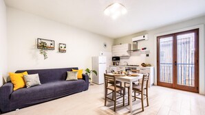 Ein kompakter Wohnbereich mit Sofa, Esstisch, Stühlen, einer Küchenzeile und einer Glastür, die zu einem Außenbereich führt.