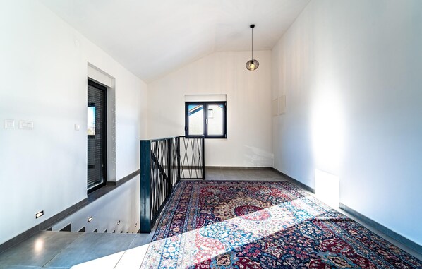 A spacious hallway with a patterned carpet, a staircase with a metal railing, and a window with blinds. - Nice home in Pridraga (Pridraga)