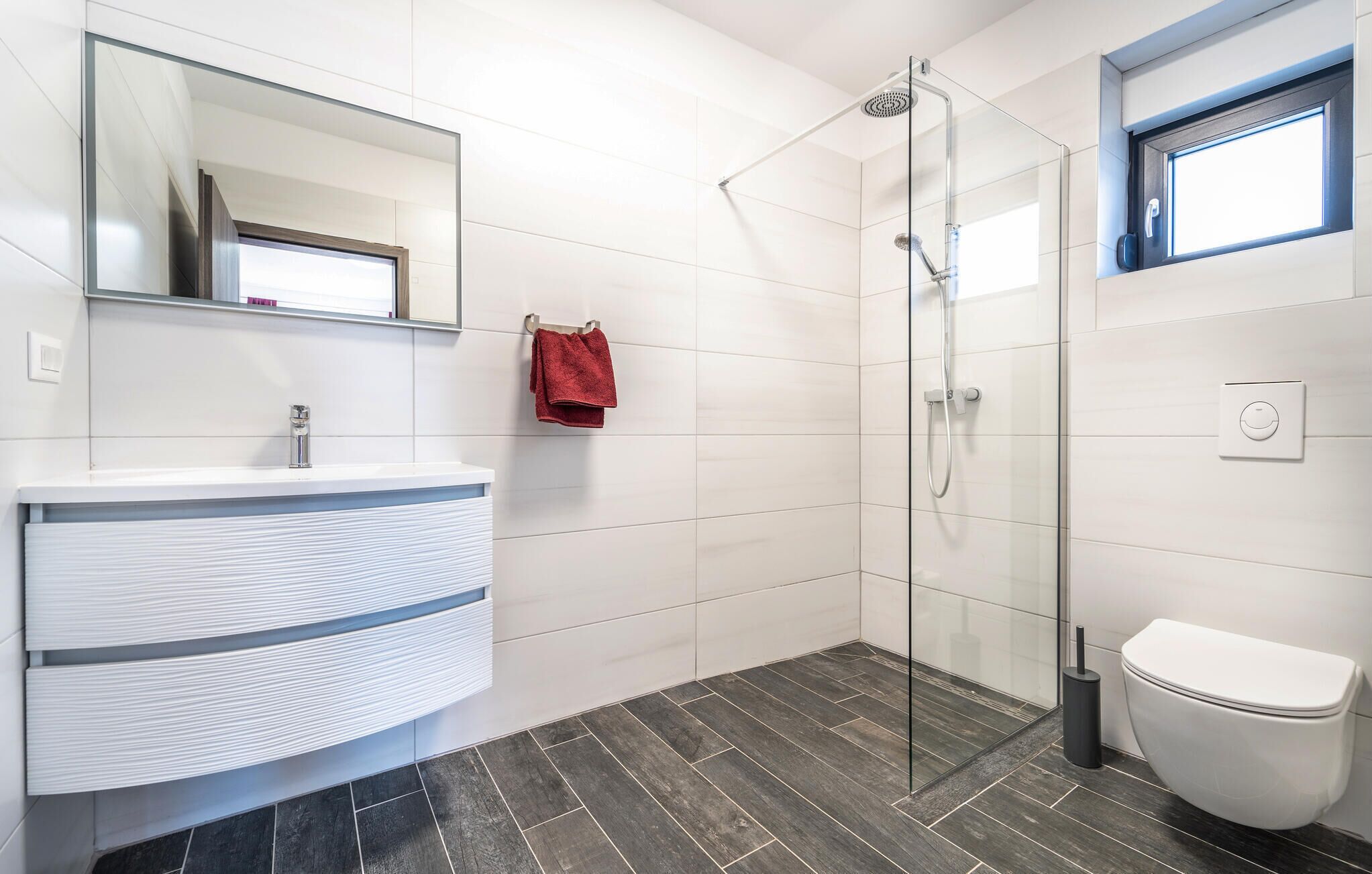 Un bany modern amb un moble de bany blanc, una cabina de dutxa de vidre i un vàter.
