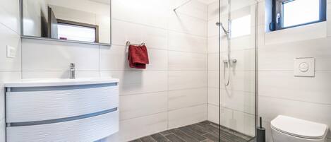 Un bany modern amb un moble de bany blanc, una cabina de dutxa de vidre i un vàter.