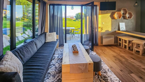 Een moderne woonkamer met een bank, een salontafel en een uitzicht op een tuin door grote ramen.