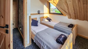 Een compacte houten kamer met twee eenpersoonsbedden, een klein raam en een deur naar buiten.