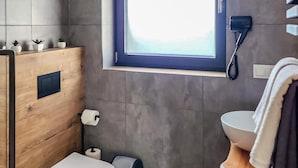 Een moderne badkamer met een houten wastafel, toilet, bidet en een raam met een telefoon.