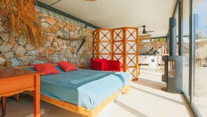 Une chambre avec un mur en pierre, un lit avec des oreillers rouges, une table en bois et une vue sur l’extérieur.