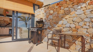 Une terrasse extérieure avec un mur en pierre, un barbecue, une table et une chaise.