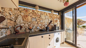 Une cuisine avec un mur en pierre, un lave-linge et une vue sur l’extérieur.