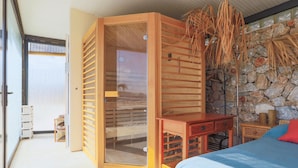 Une pièce dotée d’une grande porte coulissante, d’un mur en pierre, d’un lit avec un matelas bleu et d’une table de chevet en bois.