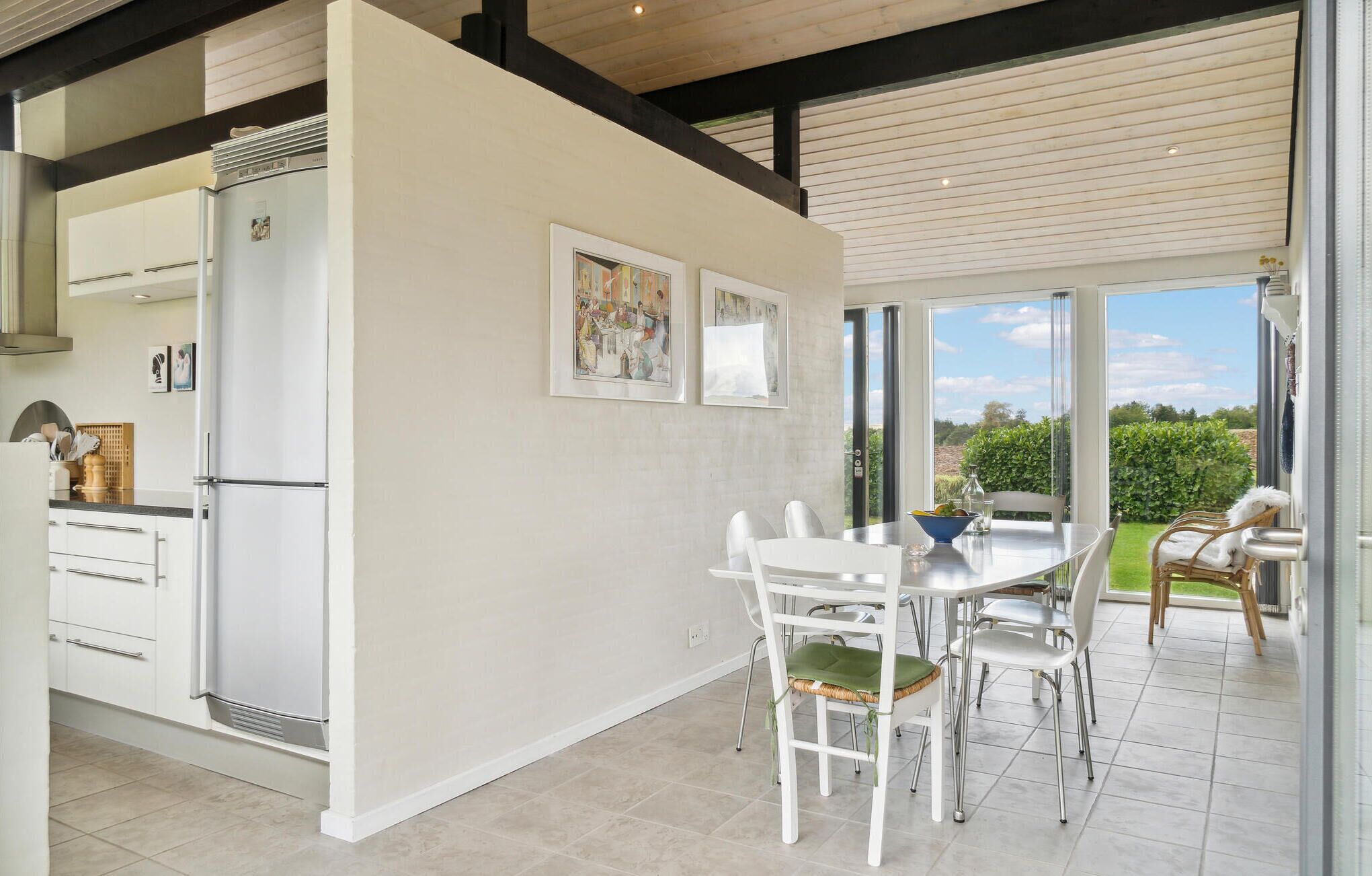 A modern kitchen with white cabinetry, a dining area with a white table and chairs, and a view of a garden through large windows.