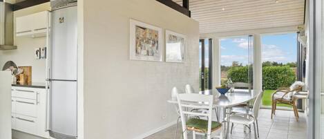 A modern kitchen with white cabinetry, a dining area with a white table and chairs, and a view of a garden through large windows.