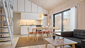 Moderni keittiö, jossa on valkoiset kaapit, ruokailutila puutuoleilla ja -pöydällä sekä suuri ikkuna, josta on näkymä ulos.