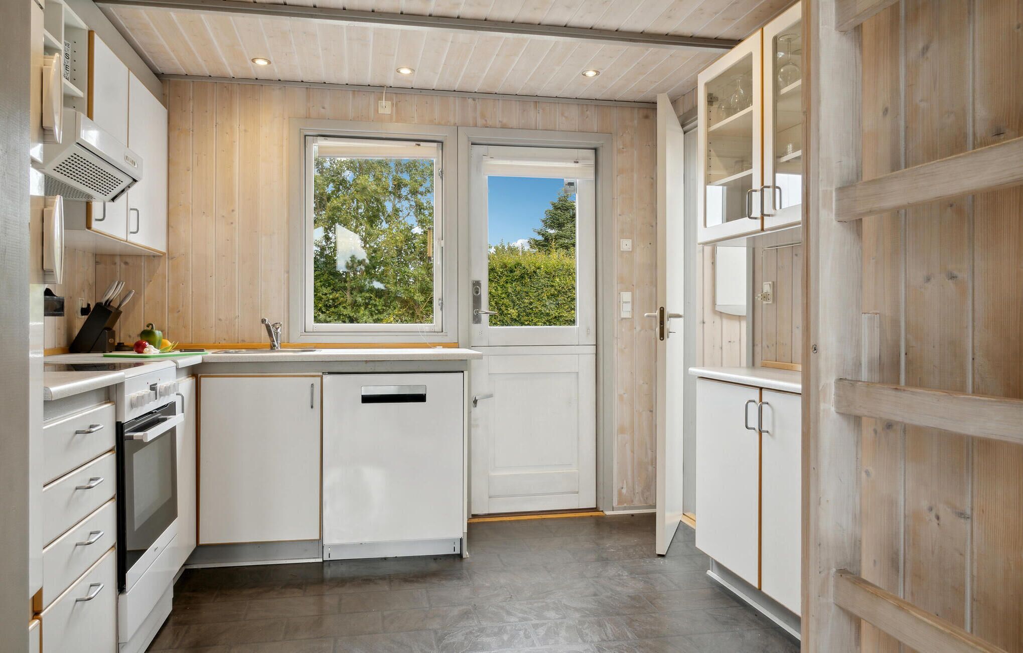 Eine moderne Küche mit weißen Schränken, einem eingebauten Ofen und einem Fenster mit Blick auf Grünflächen.