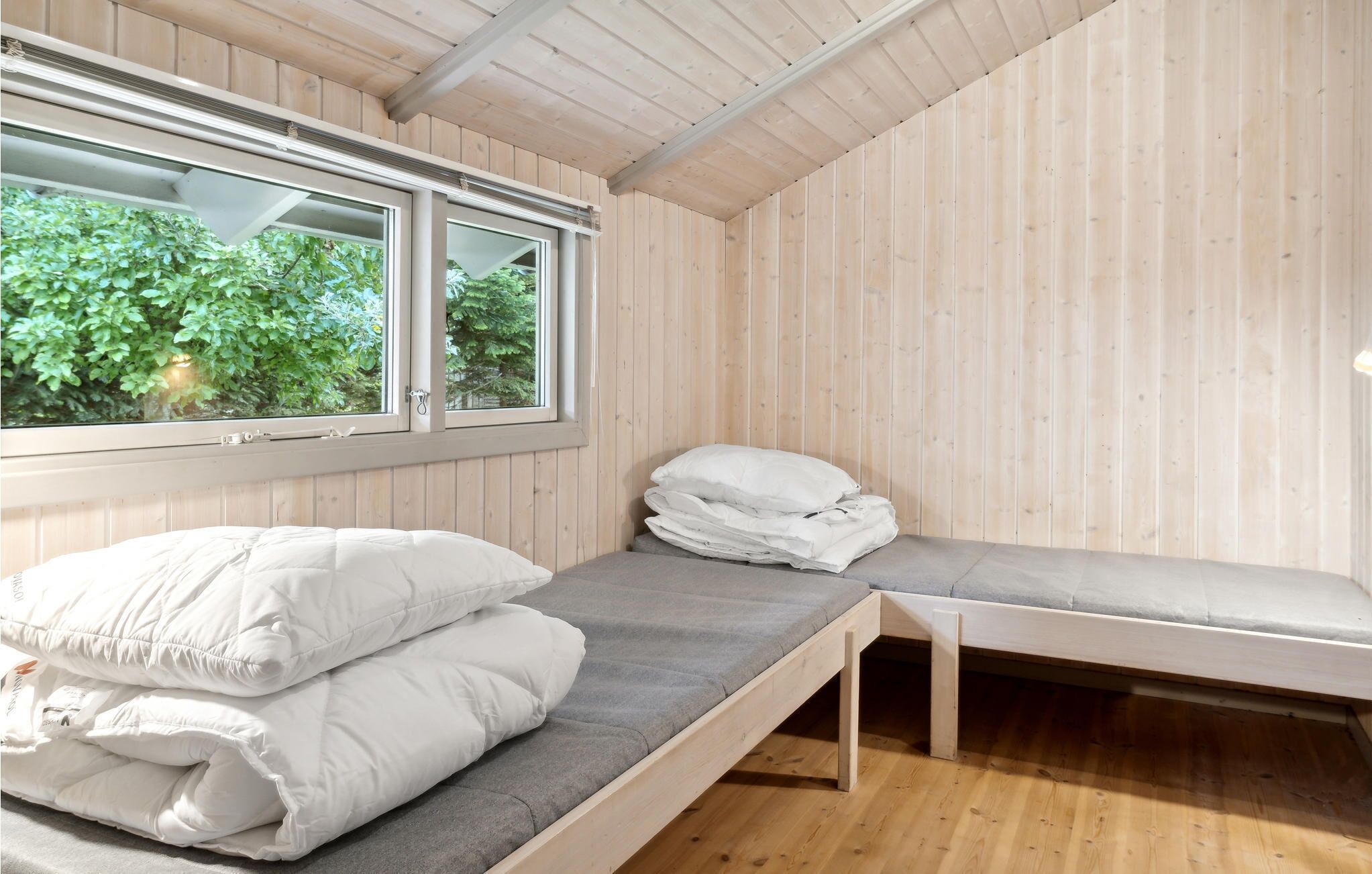 Ein kleiner Raum mit Holzwänden, einem Bett, einer Sitzbank und einem Fenster mit Blick auf Grünflächen.