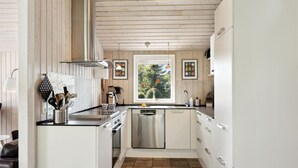 Une cuisine moderne avec des meubles blancs, des appareils en acier inoxydable et une fenêtre donnant sur les arbres.