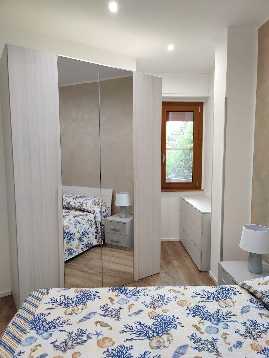 A bedroom with a bed, a nightstand, a dresser, a window, and a wardrobe.