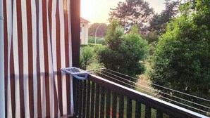 Un balcon avec un rideau à rayures, un plancher en bois et une vue sur un jardin et des arbres.