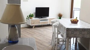 Un salon moderne avec un plancher en bois, une table à manger avec des chaises, un téléviseur et une lampe sur une table d’appoint.