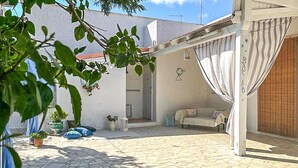 A courtyard with a stone floor, a covered seating area with cushions, potted plants, and a white wall with a door. - Beautiful home in Torre Colimena with WiFi (Torre Colimena)