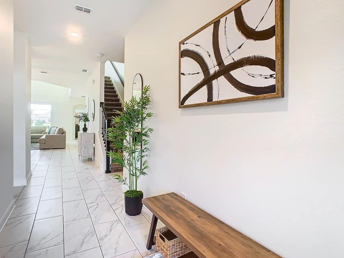 Un couloir avec un banc en bois, une plante en pot et un grand tableau abstrait accroché au mur.
