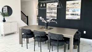Un coin repas comprenant une table rectangulaire, six chaises, un vase avec des fleurs et deux tableaux encadrés accrochés au mur.