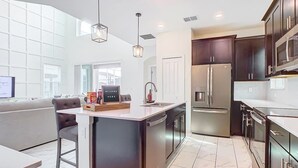 Une cuisine moderne avec des meubles de couleur sombre, des appareils électroménagers en acier inoxydable et un îlot central.