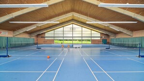 Ein Hallen-Tennisplatz mit hoher Decke und großen Fenstern.
