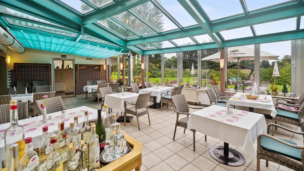 Ein Restaurant mit Glasdächern, Korbmöbeln und Blick ins Freie.