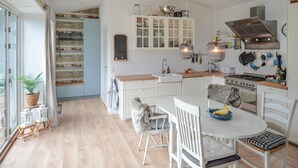 A modern kitchen with white cabinetry, a central island, and a stove. There is a dining area with white chairs and a table. - Nice home in Anholt with WiFi (Anholt)