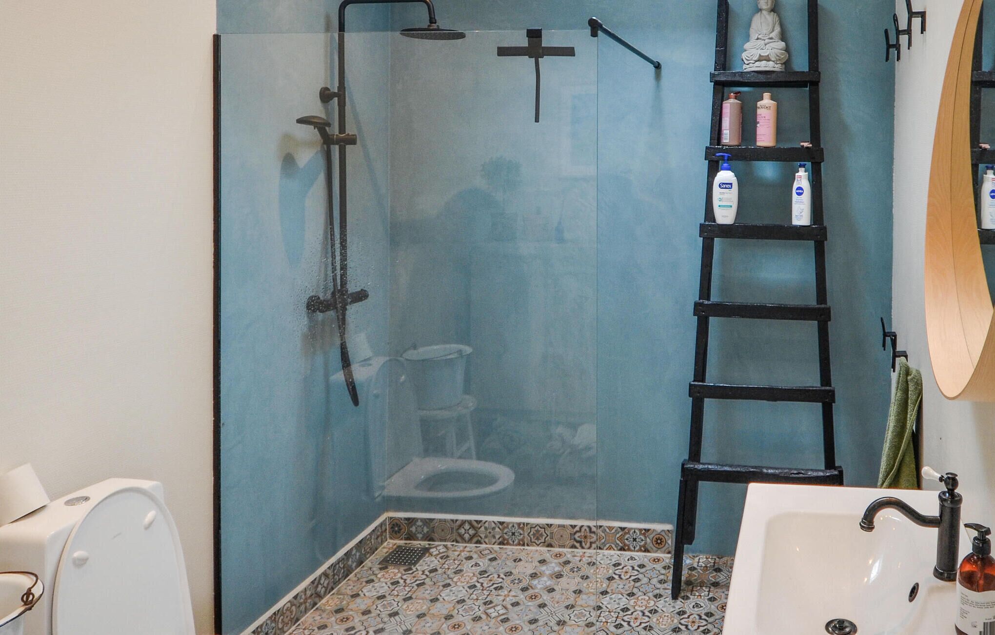 Bany amb un espai de banyera de vidre, un lavabo blanc, una estanteria de fusta en forma d'escala i un vàter.