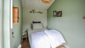 A bedroom with a bed, a nightstand, a lamp, a shelf with books and a plant, and a window with curtains. - Nice home in Anholt with WiFi (Anholt)