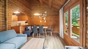 Un intérieur de chalet chaleureux avec un canapé, une table à manger, des chaises et un coin cuisine.