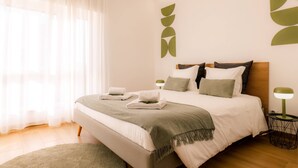 A modern bedroom with a large bed, bedside tables, and a window with sheer curtains. - Carmo House - One-bed room Apartment (Faro)