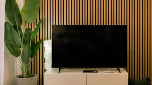 A flat-screen TV on a white cabinet against a wooden slat wall. - Carmo House - One-bed room Apartment (Faro)