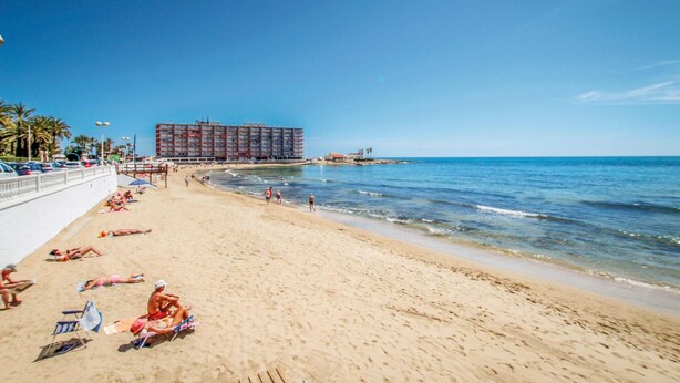 Een strand met een groot hotelgebouw op de achtergrond.