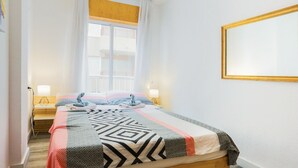 Een slaapkamer met een bed, twee nachtkastjes met lampen, een raam met gordijnen en een aan de muur bevestigd fotolijstje.
