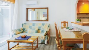 Een ruimtelijke leefruimte met een eettafel met glazen blad, een geruit sofa, een houten stoel en een spiegel aan de muur.