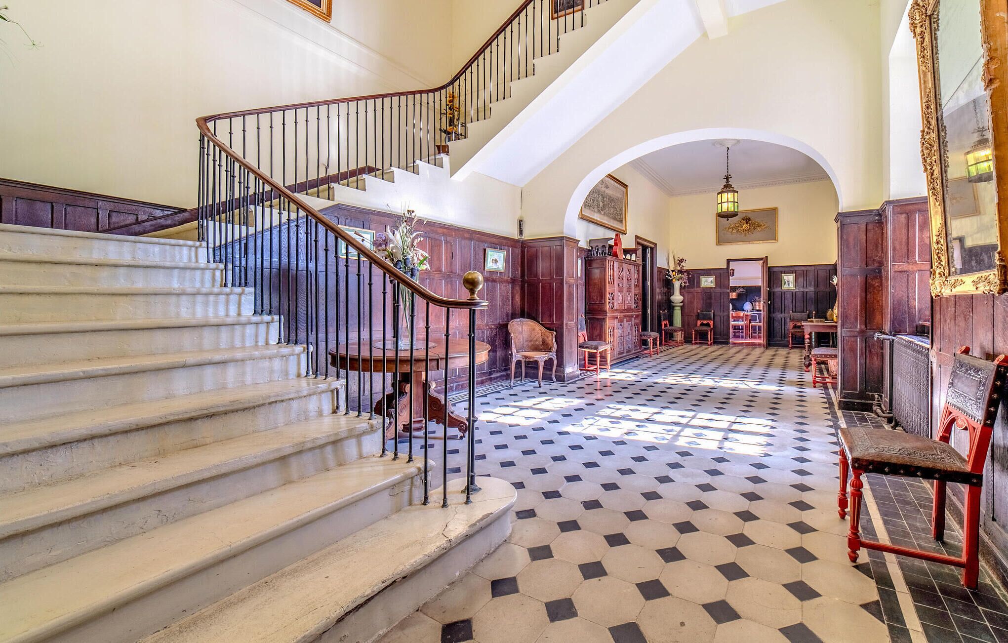 A grand staircase with a wooden railing, leading to a landing with a patterned floor.