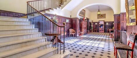 A grand staircase with a wooden railing, leading to a landing with a patterned floor.
